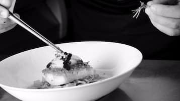 A person holding a fork and a knife over a white bowl containing food.