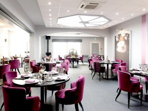 A modern dining area with round tables, pink chairs, and a central chandelier. - Logis Hôtel de France Restaurant le Lucullus (Montmorillon)