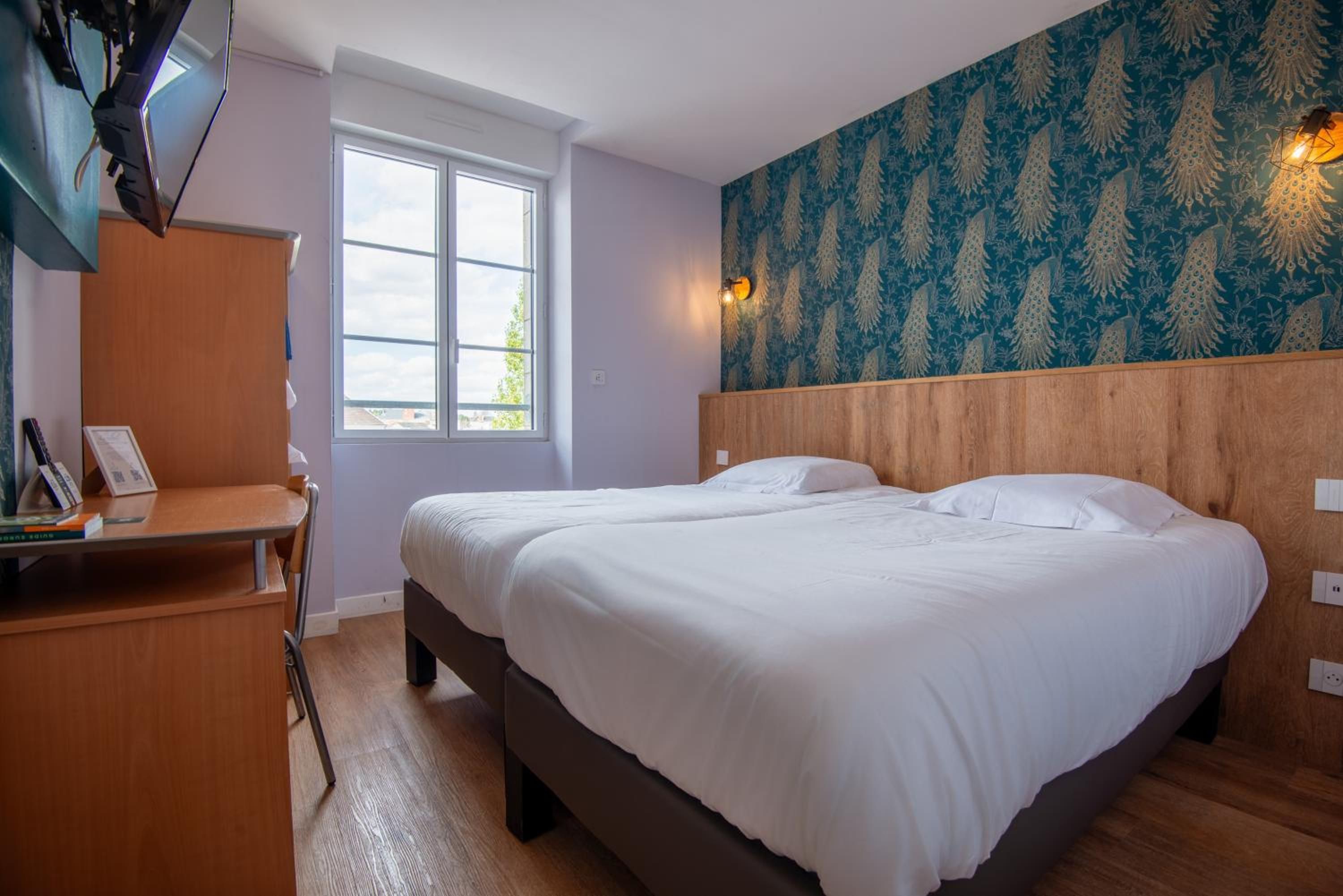 Une chambre à coucher avec un lit double, un bureau, une chaise, une fenêtre et un mur décoré d’un motif.