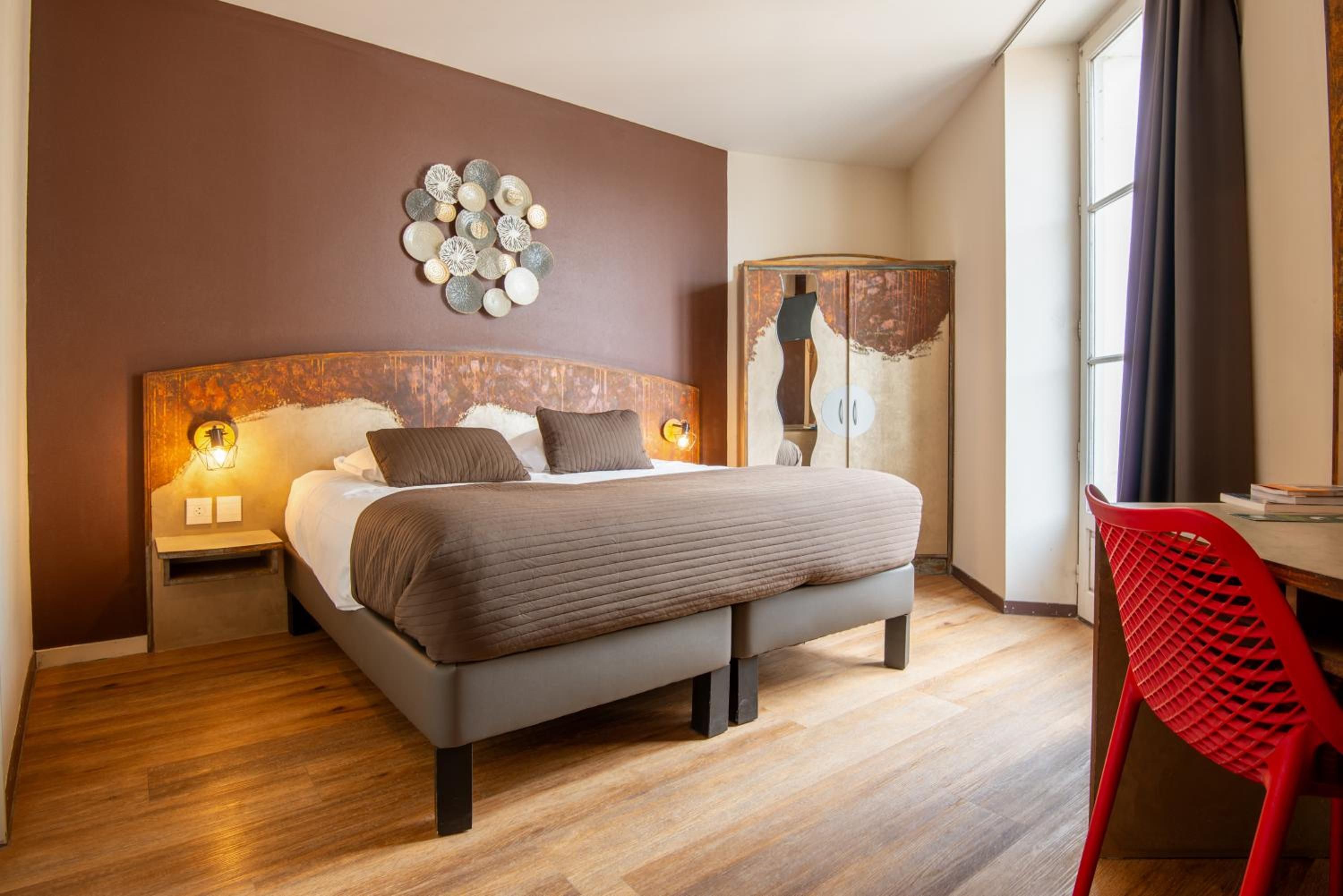 Une chambre moderne avec un grand lit, un plancher en bois, une chaise rouge et une œuvre d’art murale.