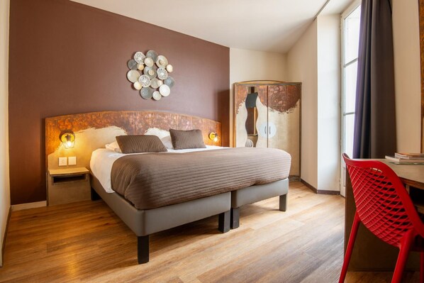 Un dormitorio moderno con una cama grande, suelo de madera, una silla roja y una obra de arte en la pared.