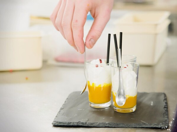 Dos vasos de postre con crema batida y un líquido amarillo, posiblemente salsa, sobre una bandeja de pizarra.