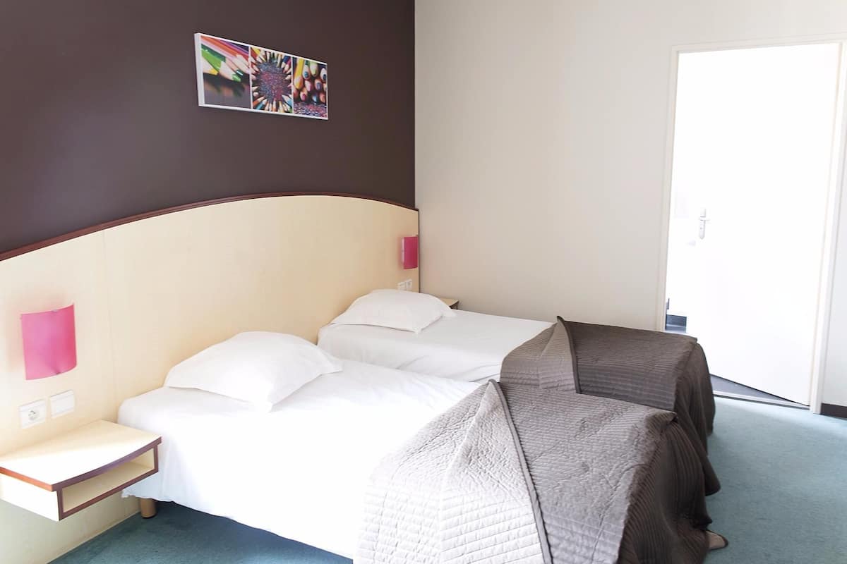 Une chambre d’hôtel avec un lit, des tables de chevet, un tableau accroché au mur et une porte.