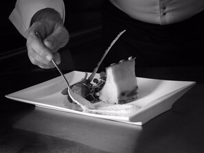 Una mano sosteniendo un tenedor sobre un plato cuadrado con un bocado de comida.