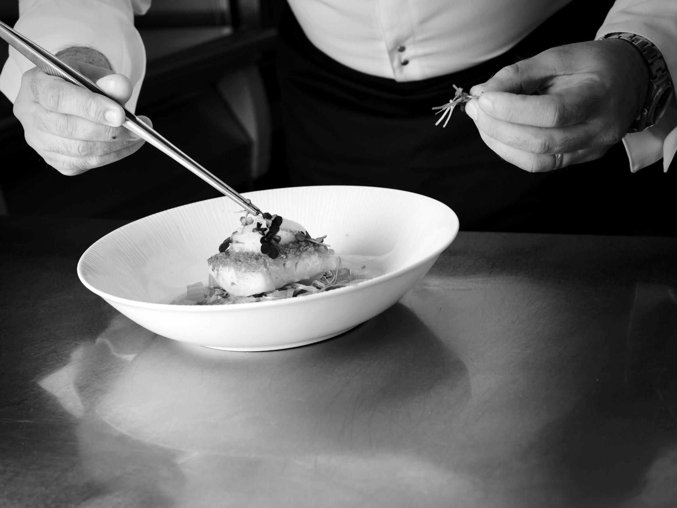 Una persona sosteniendo un tenedor y un cuchillo, a punto de comer de un tazón blanco sobre una mesa.