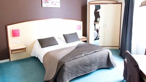 Una habitació d'hotel amb un llit, taules de nit, un armari i un quadre al mur.