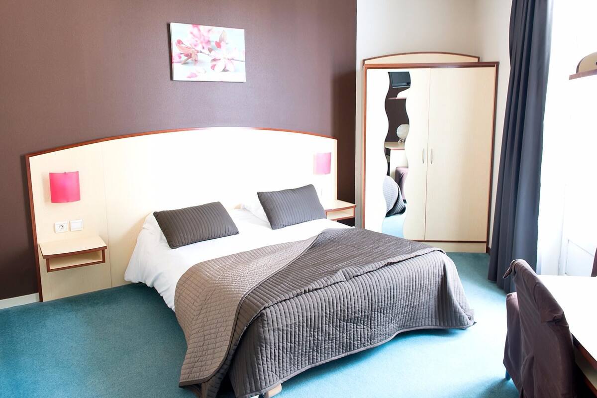Une chambre d’hôtel avec un lit, des tables de chevet, une armoire et un tableau au mur.