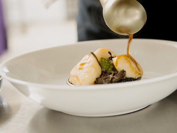 A white plate with a dish consisting of a scoop of ice cream, a piece of meat, and some greens, with sauce being poured over it. - Logis Hôtel de France Restaurant le Lucullus (Montmorillon)