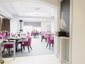 A modern dining area with round tables and chairs, a ceiling with recessed lighting, and a large portrait on the wall. - Logis Hôtel de France Restaurant le Lucullus (Montmorillon)