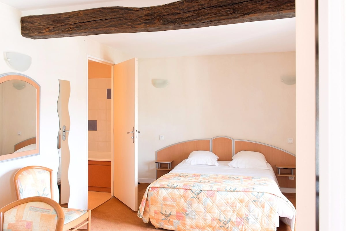 Un dormitorio con cama, una silla, un espejo y techo con vigas de madera.