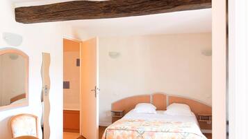A bedroom with a bed, a chair, a mirror, and a wooden beam ceiling.