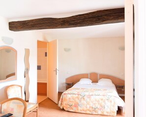 Un dormitorio con cama, una silla, un espejo y techo con vigas de madera.