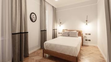 A bedroom with a wooden bed, white bedding, a headboard, two bedside lamps, and a large window with sheer curtains.
