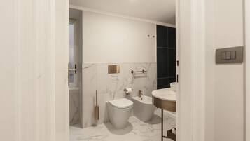 Un baño moderno con inodoro, bidé y lavamanos, suelo de mármol y pared blanca con interruptor de luz.
