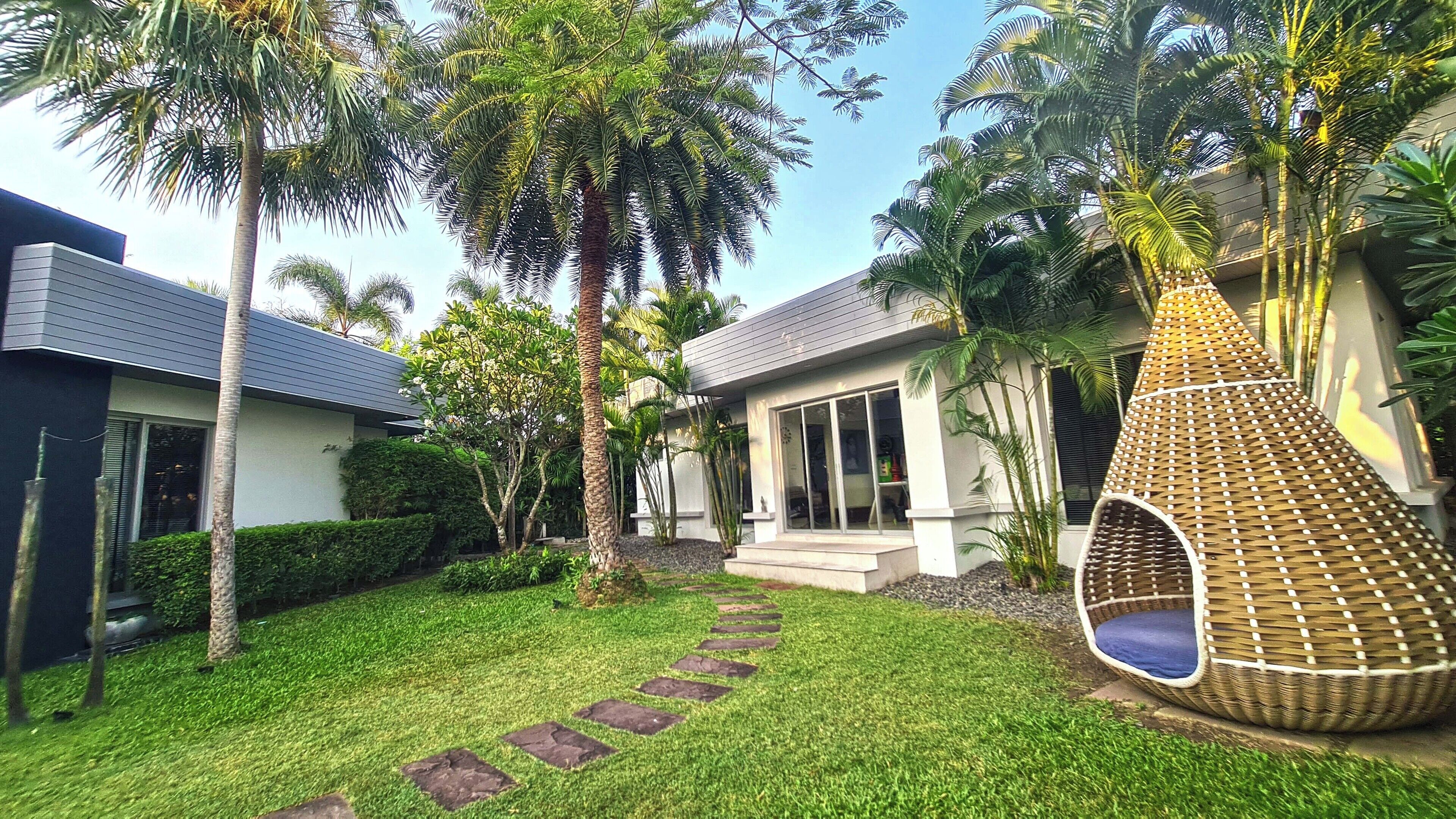 A modern house with a well-maintained garden, a stone pathway, and a hanging chair.