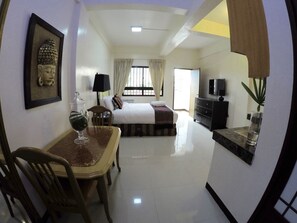 A hotel room with a bed, a desk with a chair, a TV, and a plant. - OYO 134 The Bedstation (Mandaluyong)