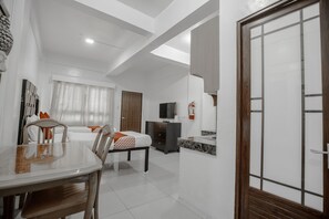 A modern hotel room with a dining area, a bed with a wooden headboard, a TV, and a bathroom with a mirror and sink. - OYO 134 The Bedstation (Mandaluyong)