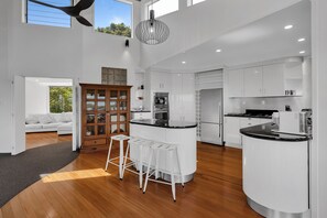 A modern kitchen with white cabinetry, a central island, and bar stools. - Double Bay Hideaway - Kerikeri Holiday Home (Kerikeri)