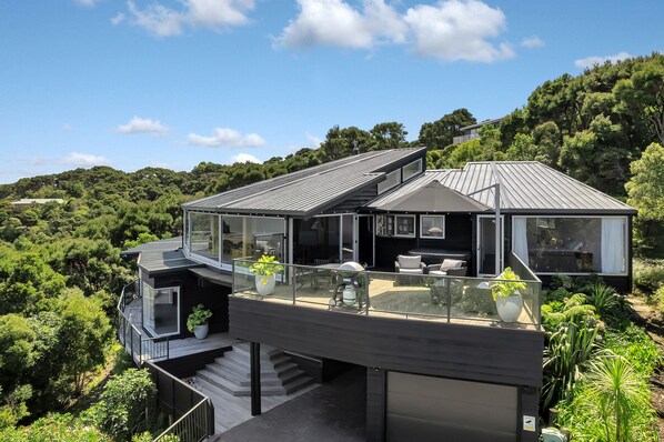 A modern house with a glass balcony, a garage, and a view of the surrounding forest. - Double Bay Hideaway - Kerikeri Holiday Home (Kerikeri)