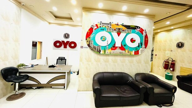 A reception area with a desk, two black leather sofas, and a large wall sign with the letters "OYO". - Super OYO 144 Al Tawasi Furnished Apartments (Salalah)