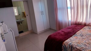 A hotel room with a bed, a wardrobe, a bathroom with a sink, and a television mounted on the wall. - Special Inn Bed and Breakfast  (Windhoek)