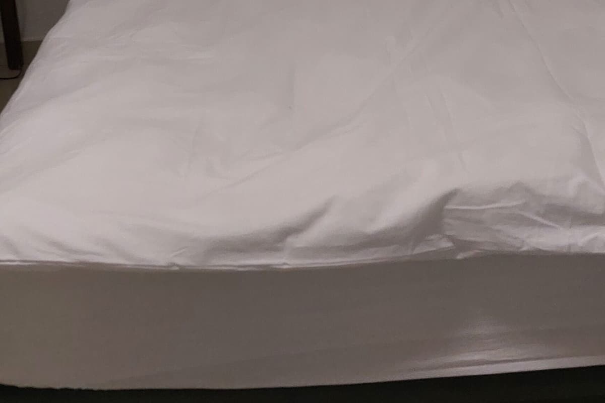 Una cama con ropa de cama blanca en una habitación con paredes lisas.