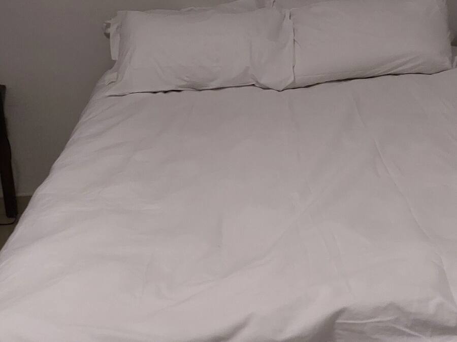 A bed with white bedding in a room with plain walls.