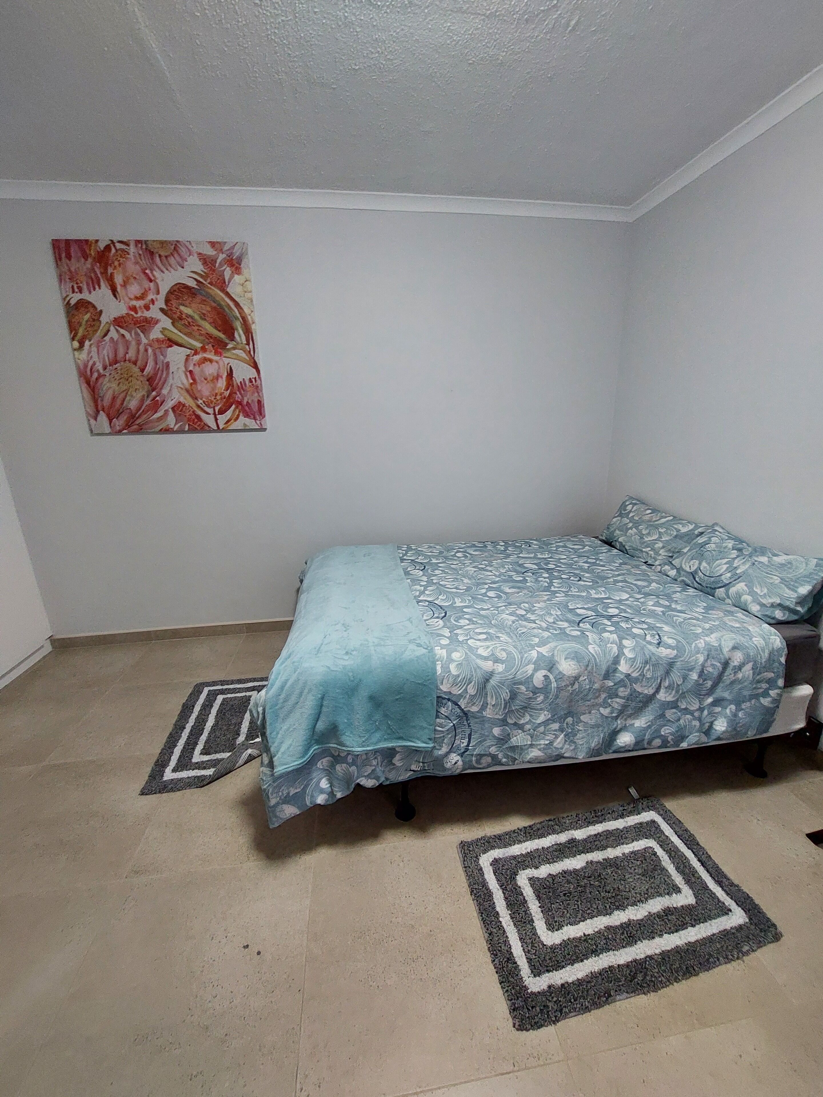 A bedroom with a bed, a floral wall hanging, and two rugs.