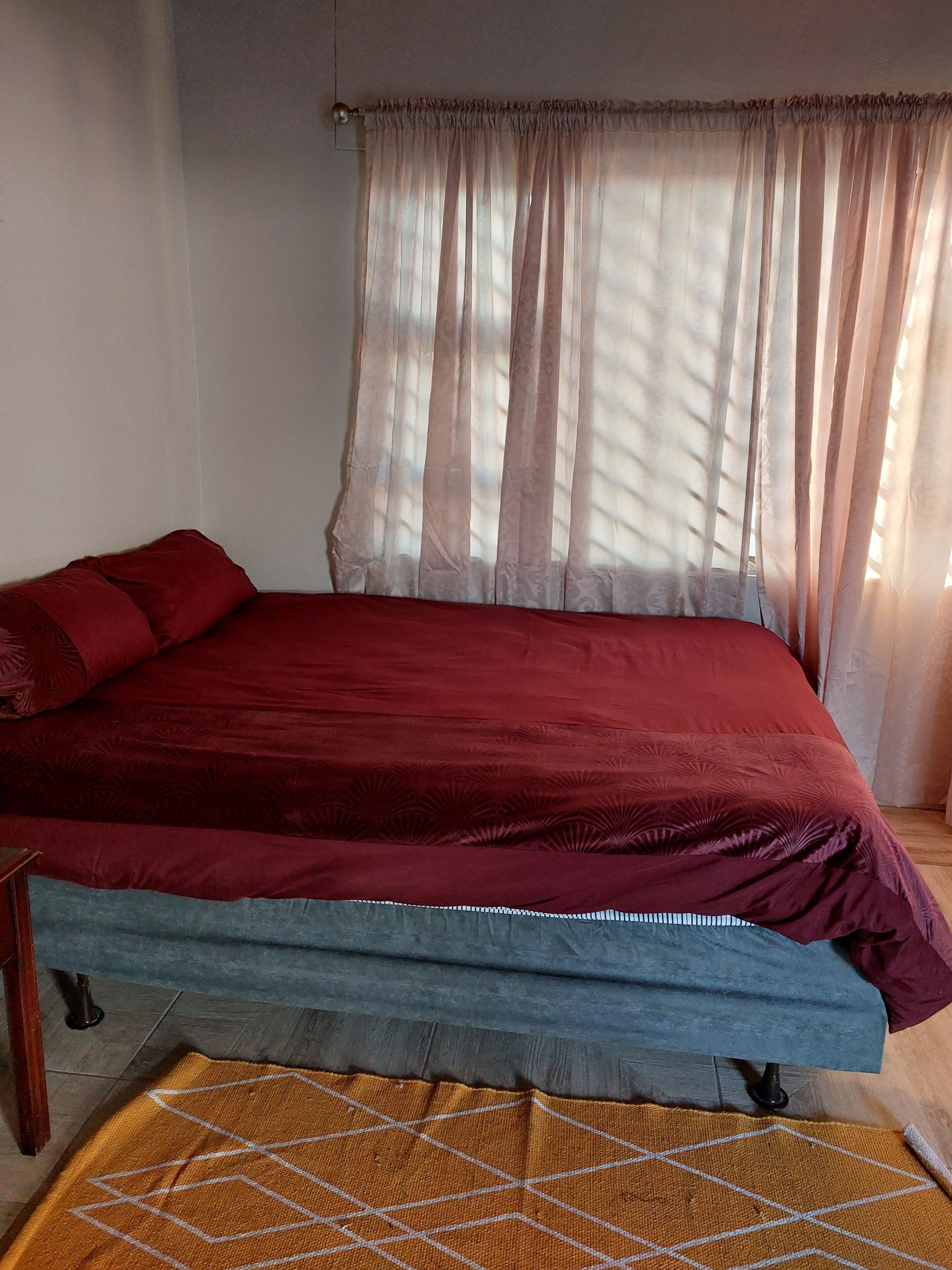 A bed with a red cover, a blue mattress, and a patterned rug.