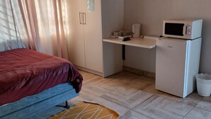 A bedroom with a bed, a desk with a microwave, a small fridge, and a TV on the wall. - Special Inn Bed and Breakfast  (Windhoek)
