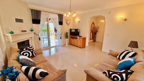 A living room with a sofa set, a TV, a fireplace, and a view through a glass door. - Private Villa ErzanMyne Private Pool Mountain View Ovacik Oludeniz (Muğla)