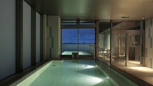 Ein moderner, überdachter Pool mit Glaswand, der eine Aussicht auf die Berge bei Nacht bietet.