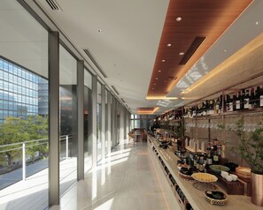 Een moderne bar met een lange toonbank, glazen ramen en uitzicht op de stad.