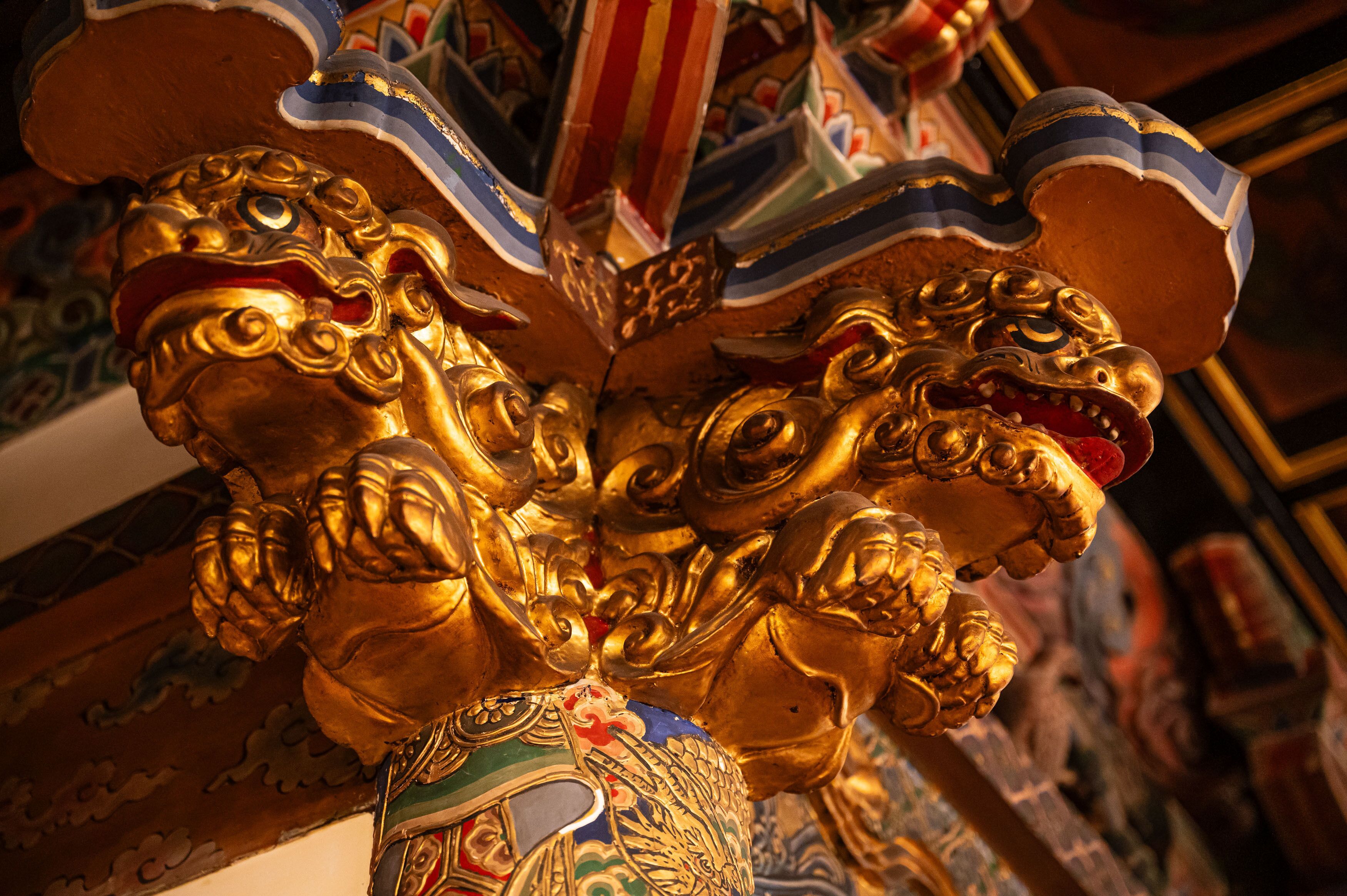 A close-up of ornate golden lion statues with intricate designs, set against a richly decorated background.