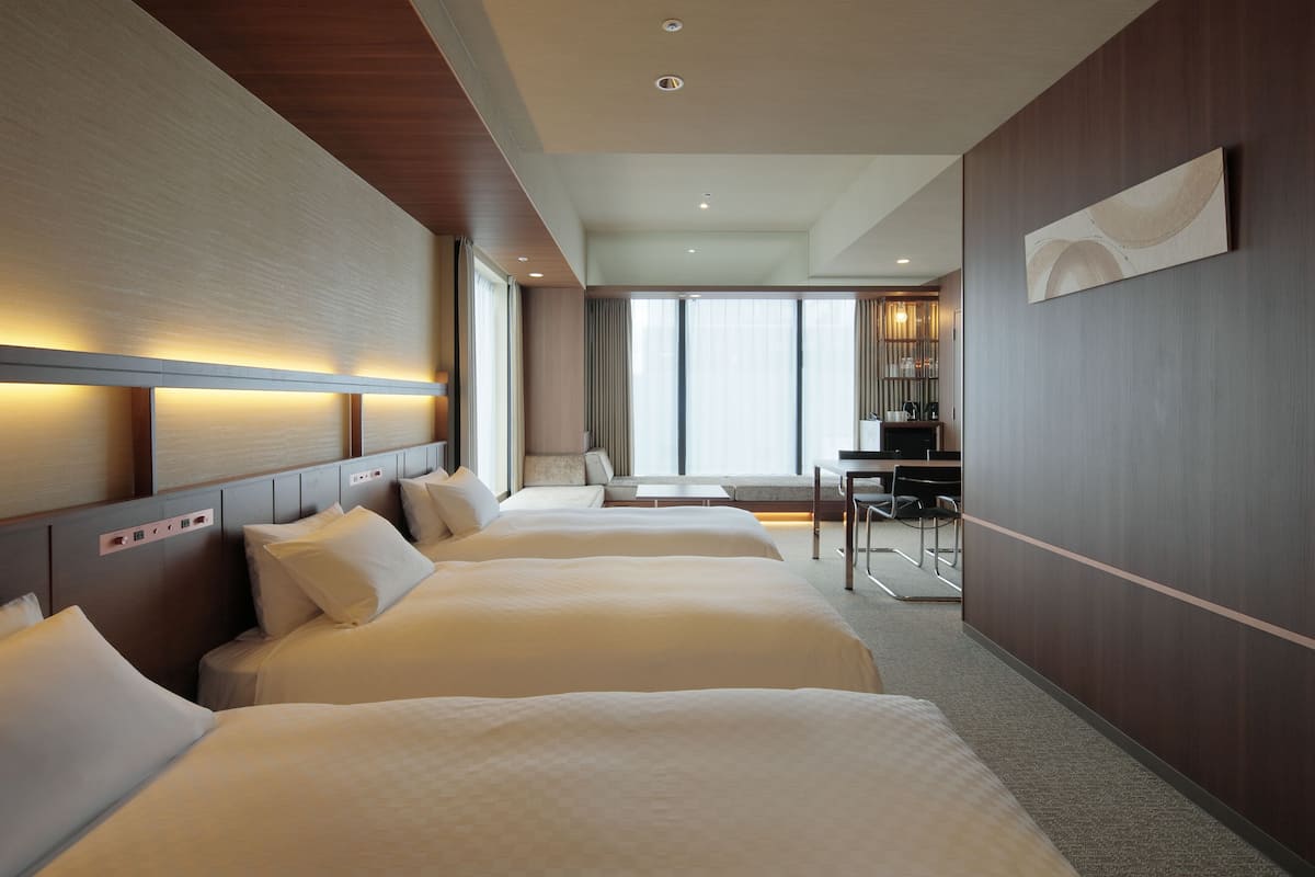 Habitación de hotel con tres camas, un escritorio y un ventanal grande.