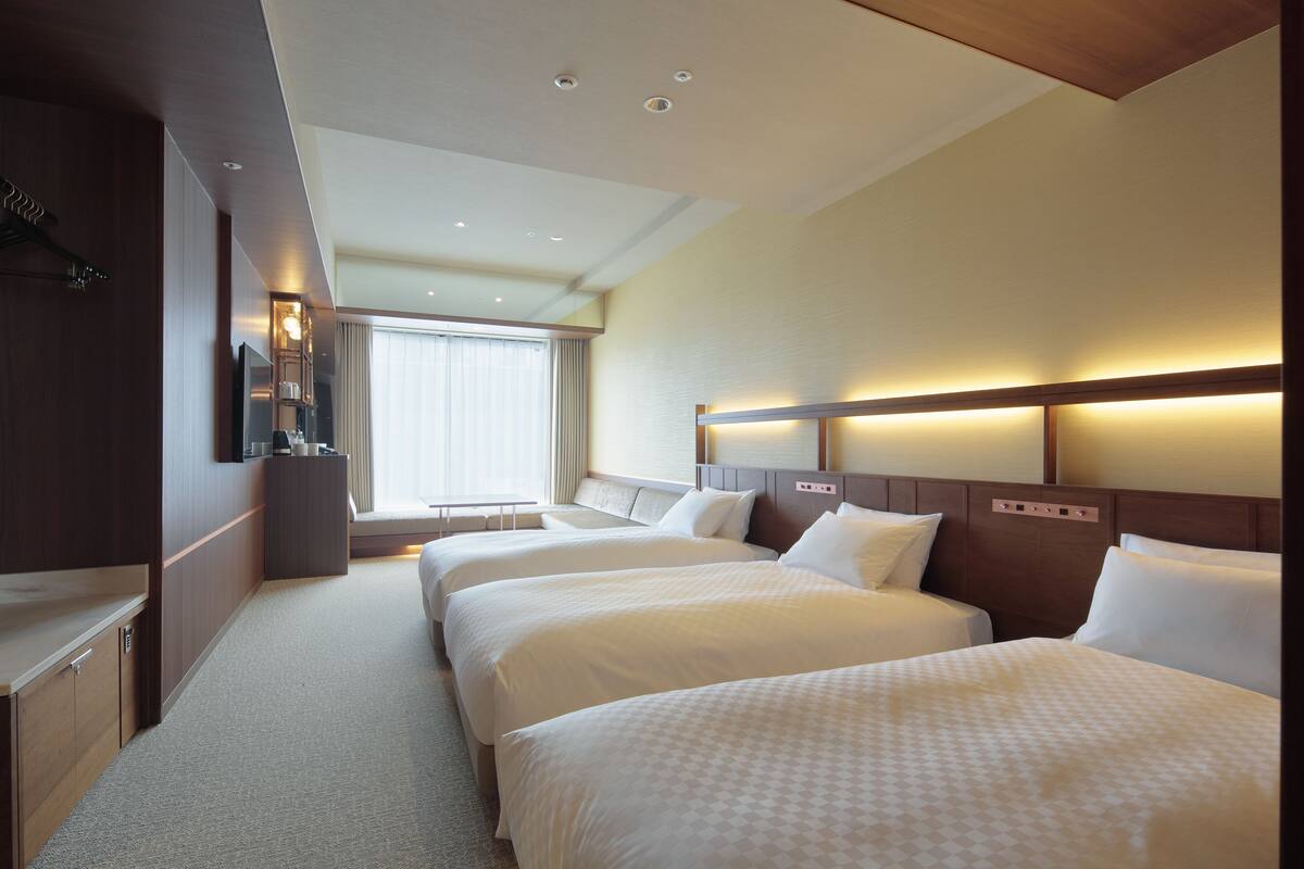 Habitación de hotel con dos camas, un escritorio, un armario y un ventanal grande.