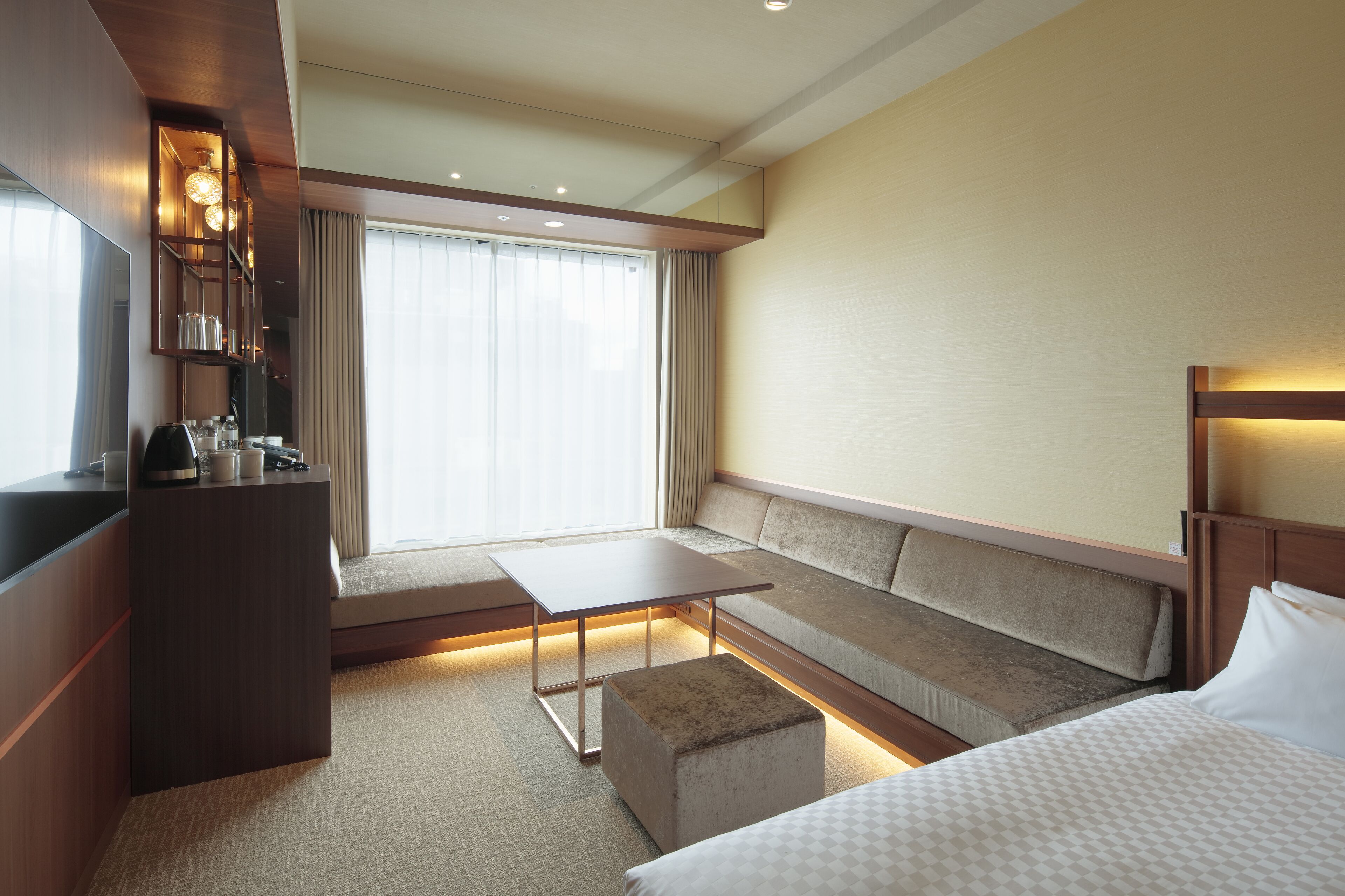 A hotel room with a sofa, a bed, a small table, a TV, and a window with curtains.