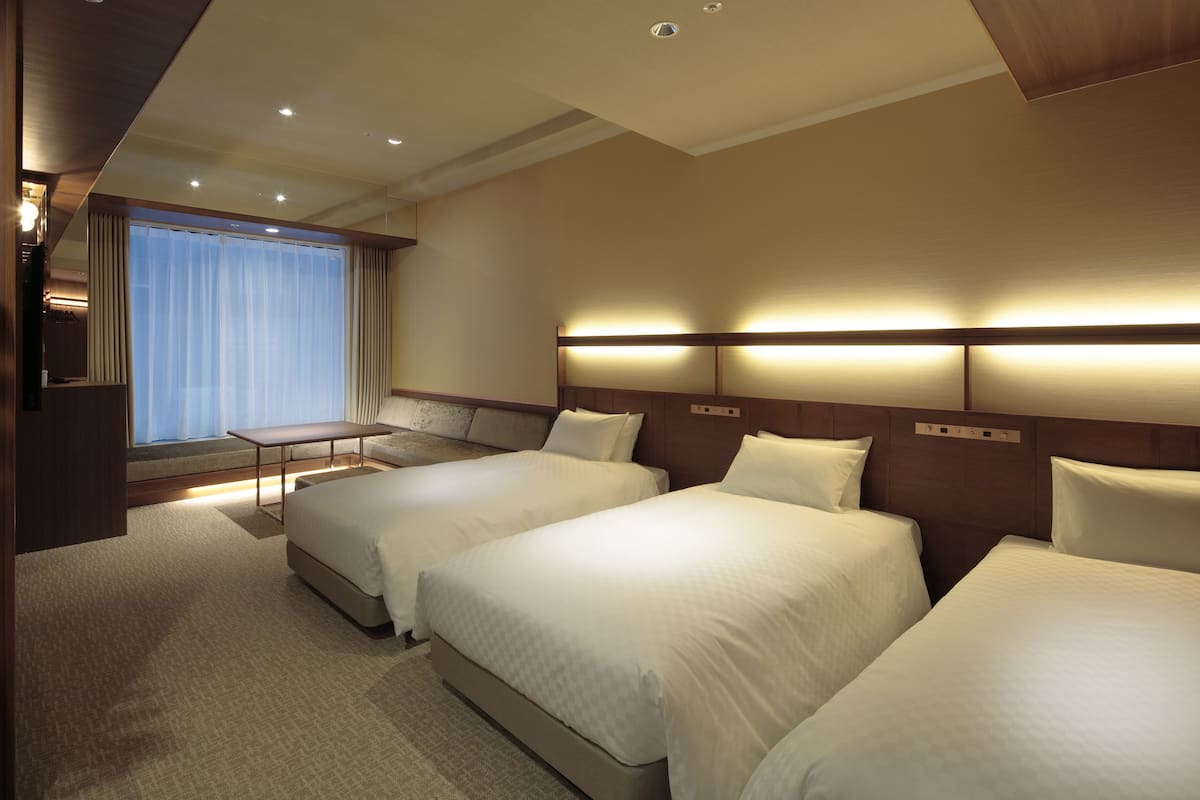 Habitación de hotel con dos camas, una mesita y un ventanal con cortinas.