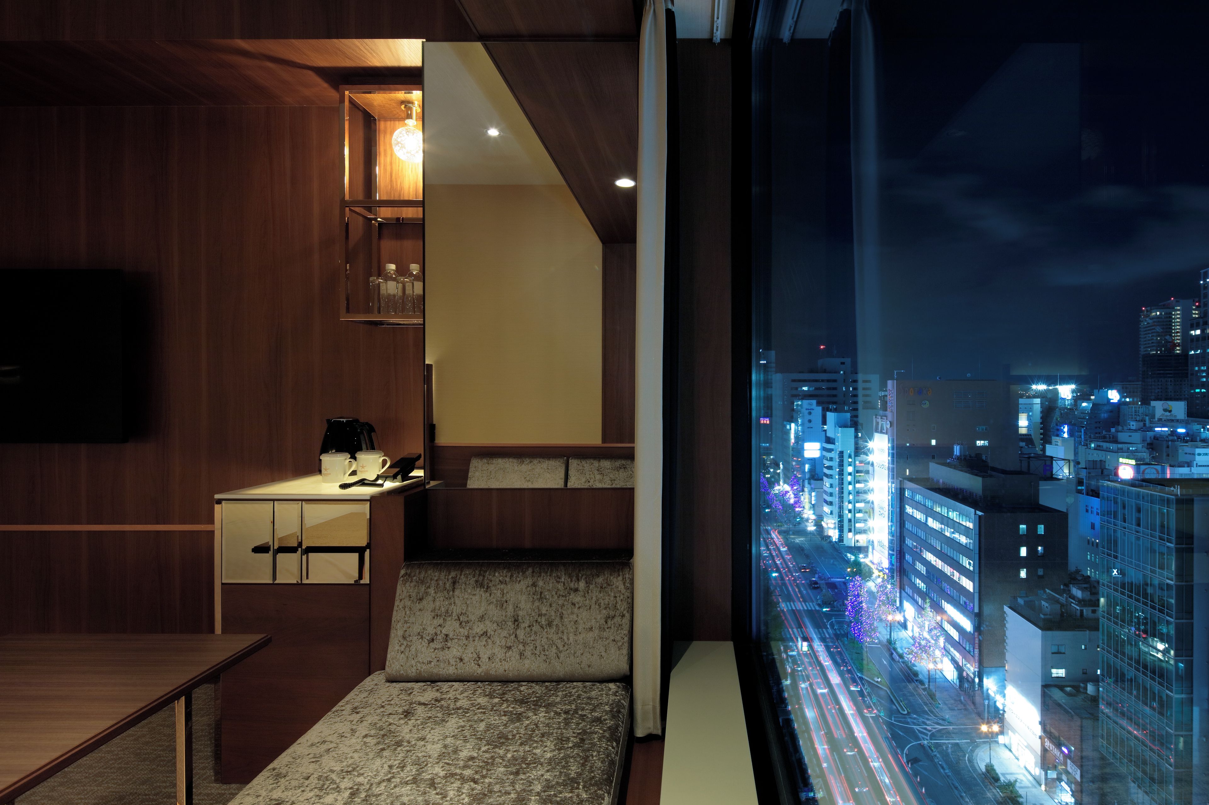 A modern hotel room with a city view, a small kitchenette, and a seating area.