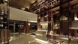 Un hall d’entrée spacieux avec un plafond haut, des étagères en bois ornées d’objets décoratifs, un coin salon et un sol réfléchissant.