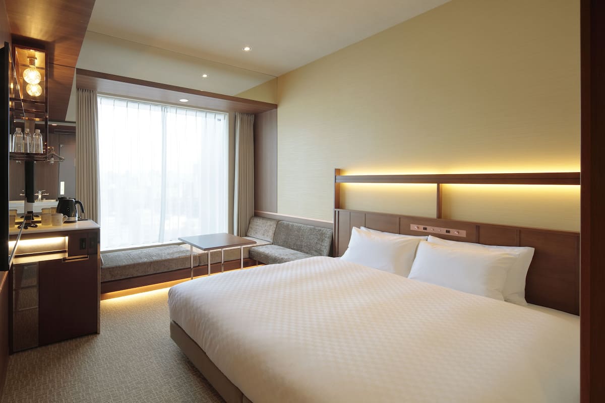 Habitación de hotel con una cama grande, un escritorio con silla, un sofá y una ventana con cortinas.