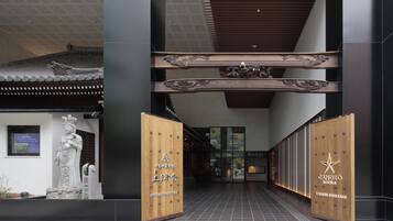 A hotel entrance with traditional architectural elements, a statue, and wooden doors with hotel branding.