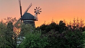 Un moulin à vent doté d’une structure en forme de dôme et de deux pales, entouré d’arbres et se dressant sous un ciel au coucher du soleil.