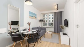 A modern living room with a dining area, grey sofa, and a large window with curtains.
