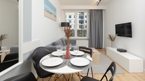 A modern living room with a dining area, grey curtains, a flat-screen TV, and a vase with dried plants.