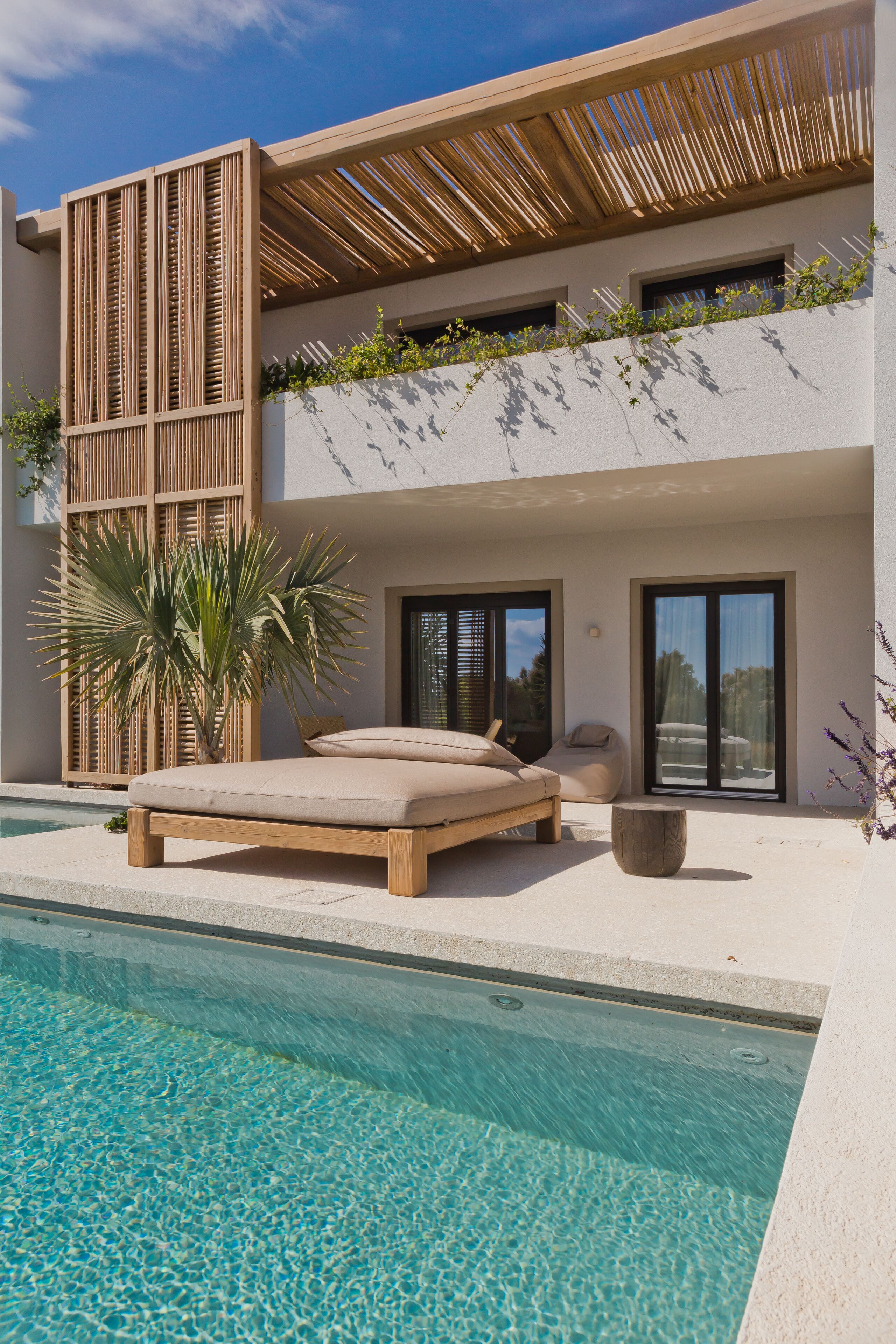 A modern poolside area with a lounge chair, a wooden pergola, and a clear pool.