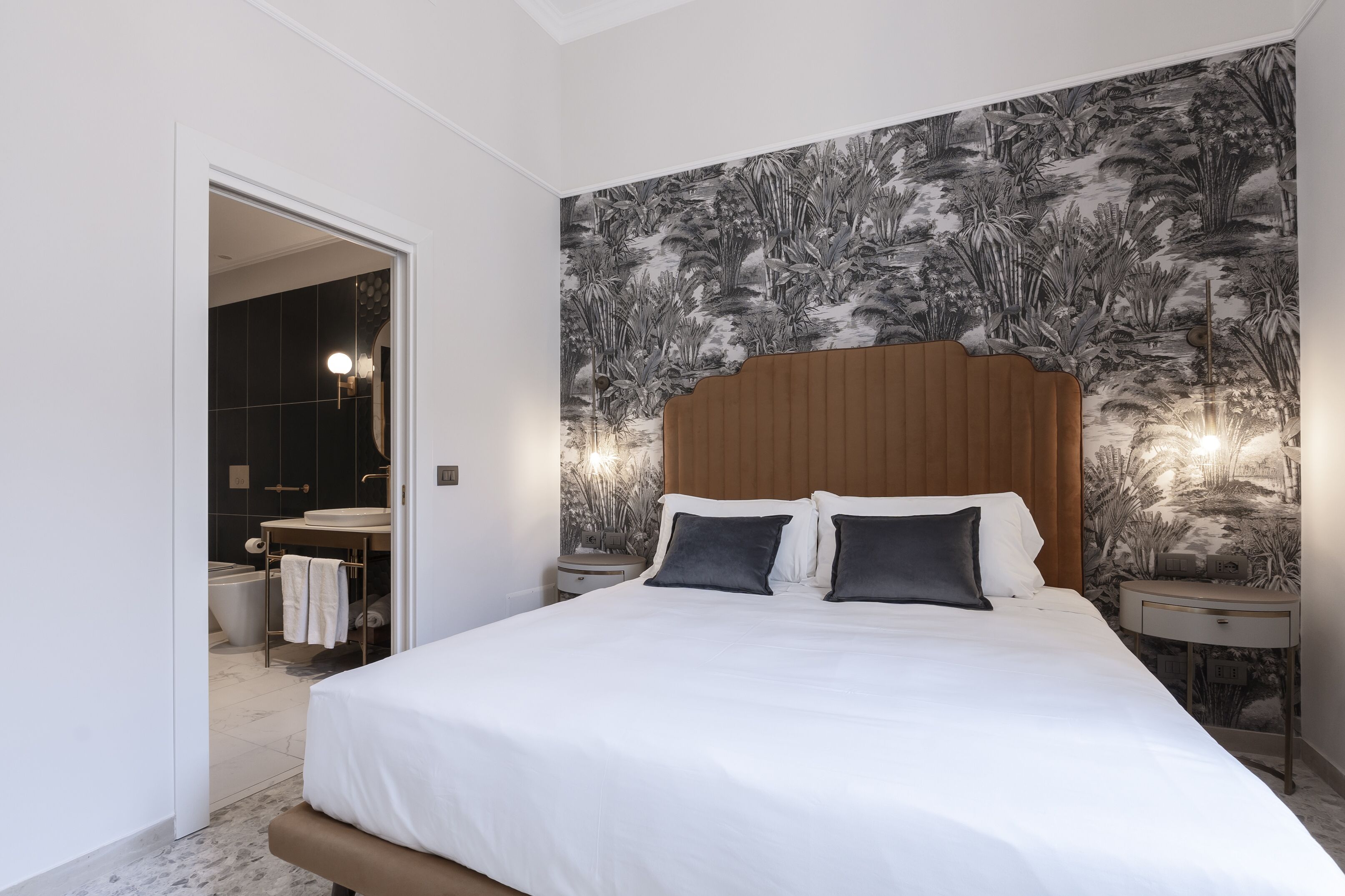 A bedroom with a large bed, a wooden headboard, and a wall with a nature-themed wallpaper.
