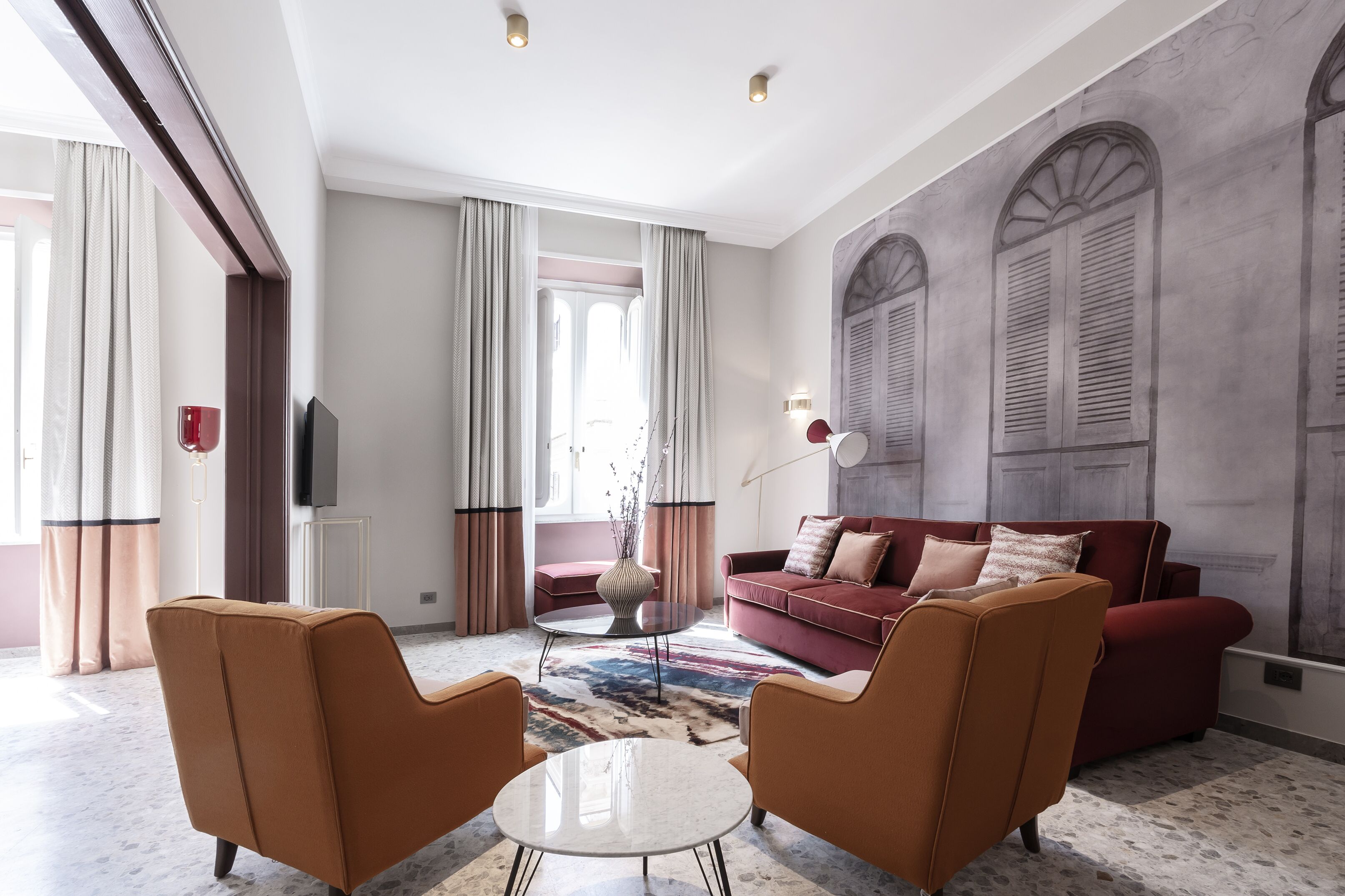 A modern living room with a red sofa, two brown armchairs, a small white table, and a patterned rug.