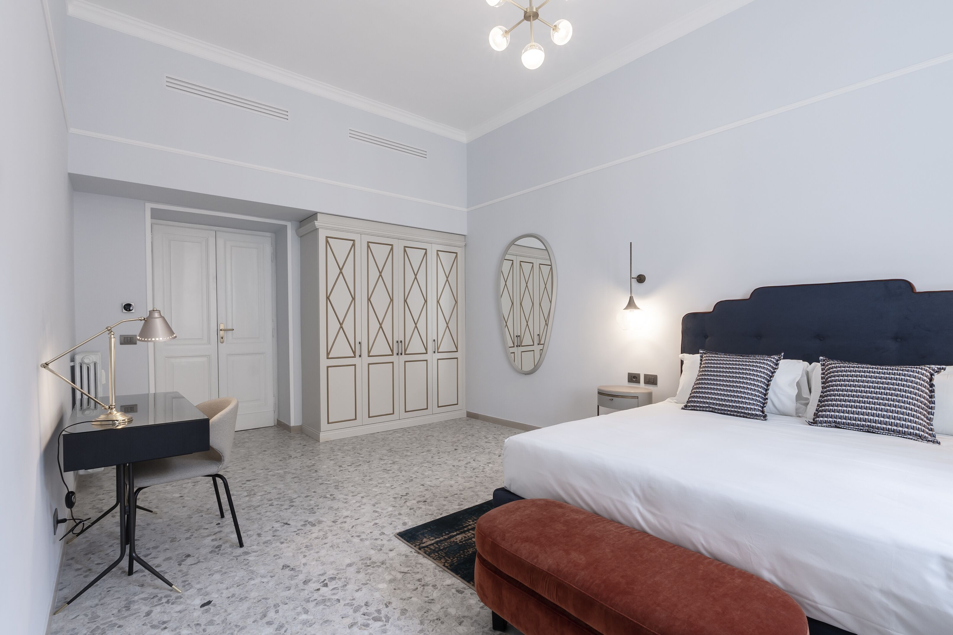 A bedroom with a bed, bedside tables, a desk, a chair, a wardrobe, and a mirror.