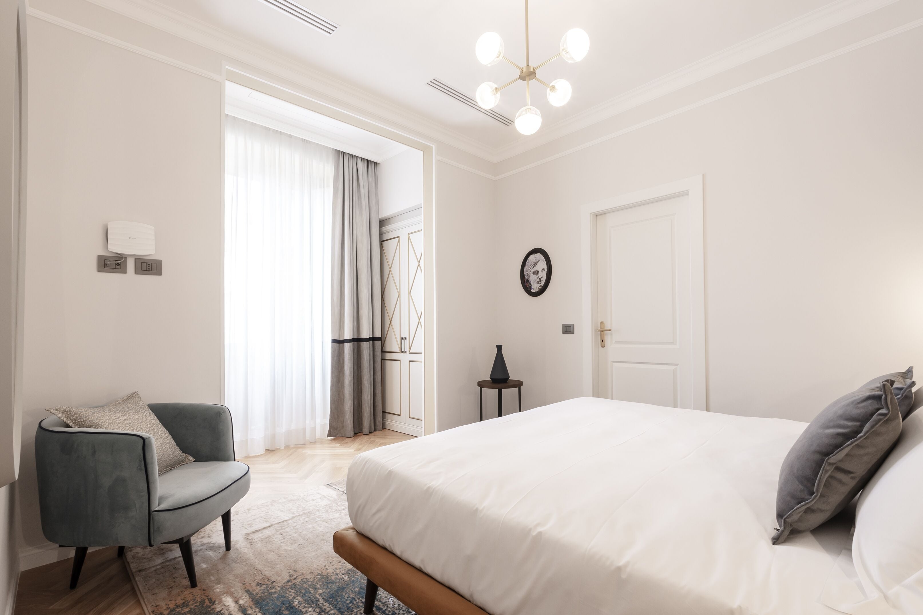 A bedroom with a large bed, a chair, a small table, and a door.